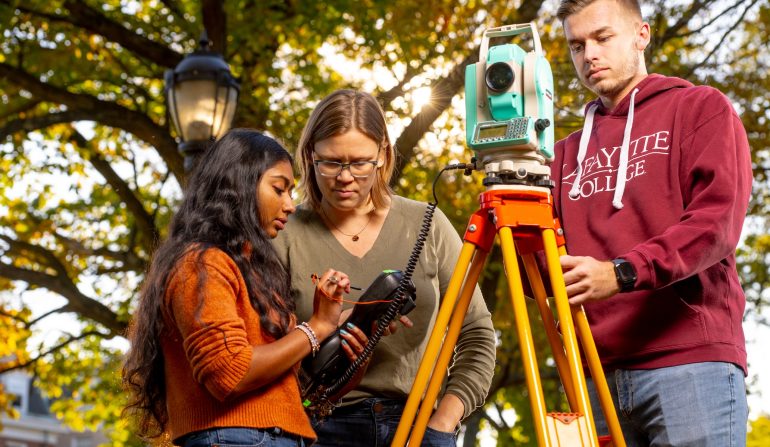 Three students using surveying equipment