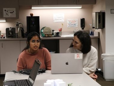 Two women sitting at a table with a laptop